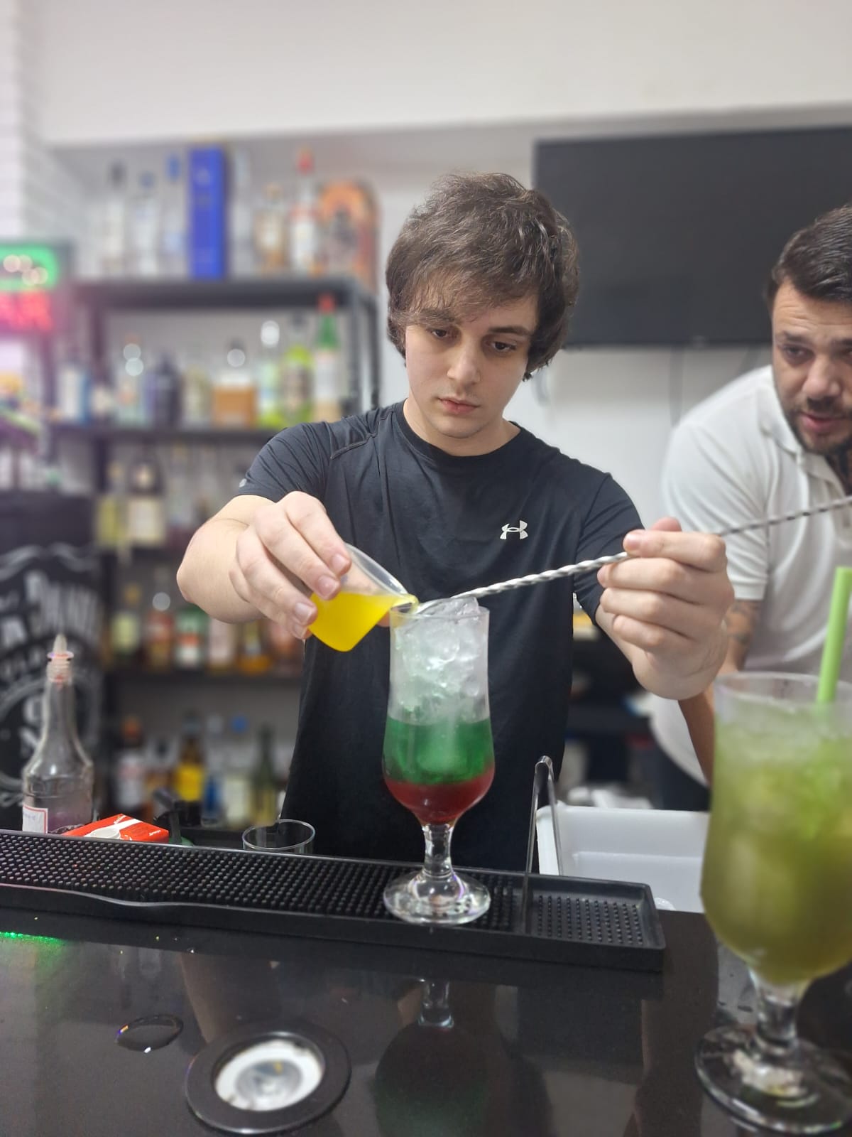Aluno preparando um coquetel em camadas na aula de coquetelaria e mixologia