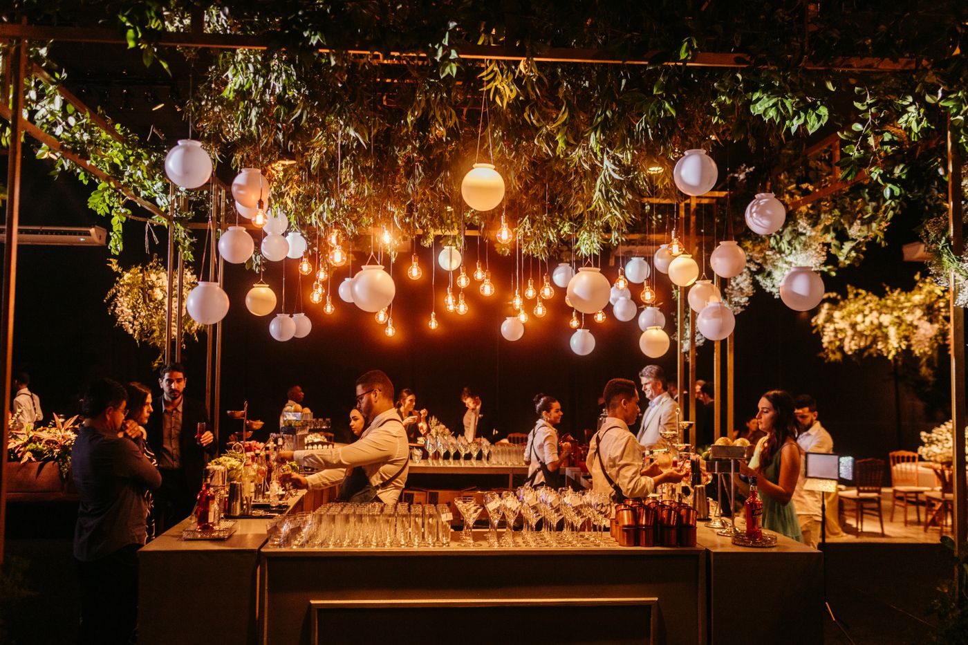 Bar decorado em recepção de casamento com iluminação ambiente e folhagens